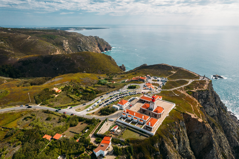 Aerial drone view of lighthouse at Cabo da Roca with unidentifiable tourists enjoying the amazing views. Guincho Beach is visible in the far background